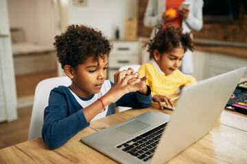 Cute black boy showing heart shape during video call over laptop at home.