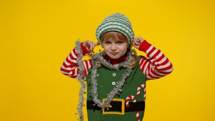 Displeased little blonde kid teen teenager girl in Christmas elf Santa helper costume isolated on yellow studio background. Child looking unhappily angry, sad at camera. Negative emotions and reaction