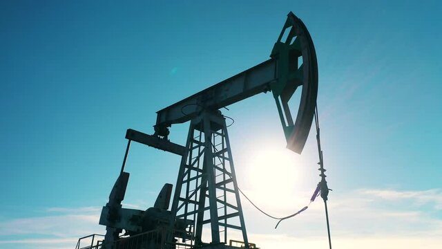 Low-angle closeup of oil pump jack moving against blue sky