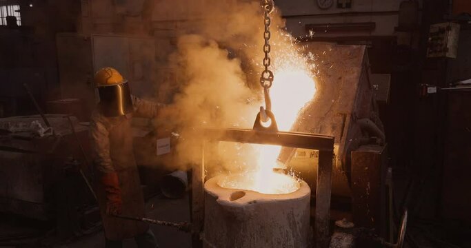 Close-up view of a factory worker pouring molten metal out a smelting furnace at a steel casting foundry