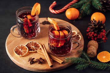 Two glasses of hot mulled wine with fruits and spices on dark background. Winter warming holiday drink.