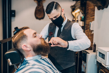 Young good looking hipste man visiting barber shop. Trendy and stylish beard styling and cut.