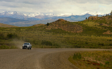 dirt road with pickup truck in the background kicking up dust snowy mountains background