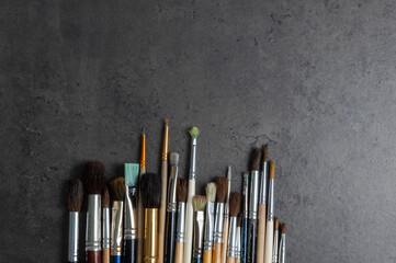 Row of artist paint brushes of various models closeup on a dark decorative stucco surface with a copy space. creative horizontal background.