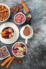 top view of herbal tea with a bowl of nut and chocolate and dry flowers on grey ground