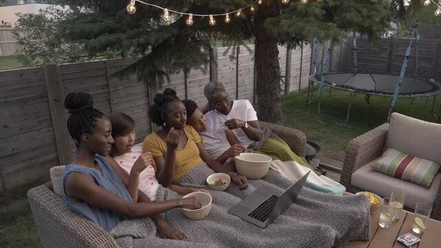 Family Watching Movie On Laptop In Backyard