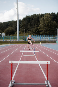 Female athlete leaping over barrier at stadium
