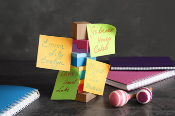 Paper notes with different baby names, toys and notebooks on grey table