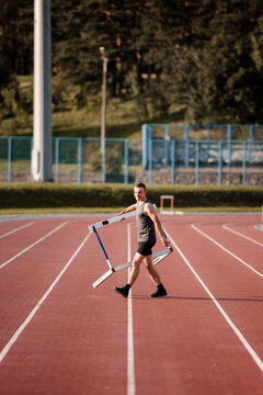 Athlete walking on race track and carrying hurdle