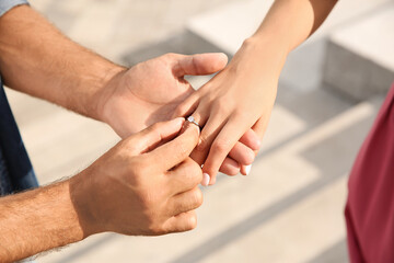 Man putting engagement ring on his girlfriend's finger outdoors, closeup