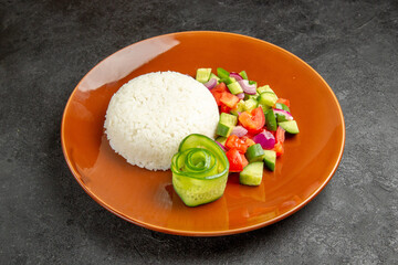 Close up view of homemade rice dish and salad with tomato and cucumber on dark background