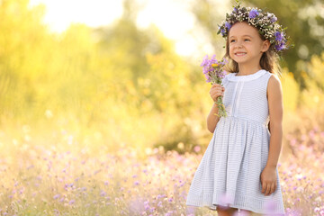 Cute little girl wearing beautiful wreath with bouquet of wildflowers outdoors, space for text. Child spending time in nature