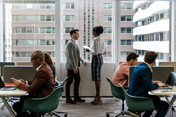 Female executive with report talking to male manager at busy office