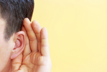 Man listens attentively with her palm to her ear on yellow background