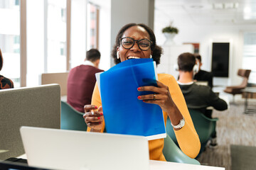 Positive woman laughing while working with laptop and documents at office