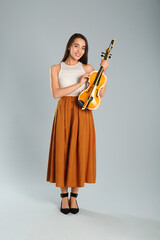 Fototapeta premium Beautiful woman with violin on grey background
