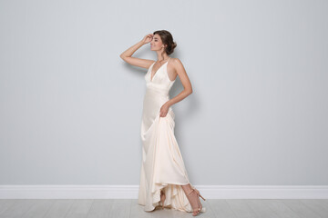 Fototapeta na wymiar Young bride wearing beautiful wedding dress near light grey wall