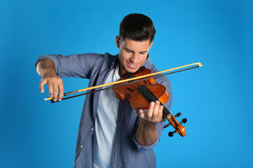 Happy man playing violin on light blue background © New Africa