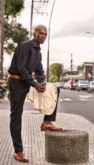 Young African-American entrepreneur with his foot on a bollard holding his jacket, looking into the distance. Lifestyle