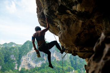 Confidence Asian woman climber with safety rope climbing high up on rocky mountain at tropical...