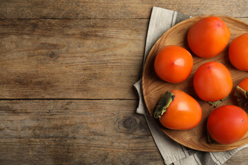 Fototapeta na wymiar Tasty ripe persimmons on wooden table, flat lay. Space for text