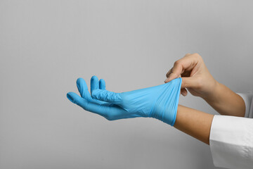 Doctor putting on medical gloves against light grey background, closeup