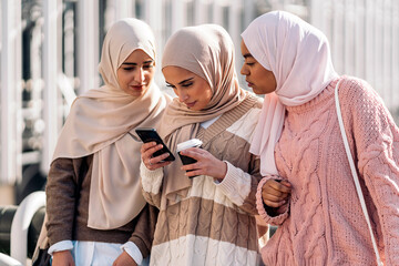 Three muslim women looking at a mobile phone.