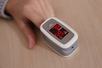 Woman measuring oxygen level with modern fingertip pulse oximeter at wooden table, closeup