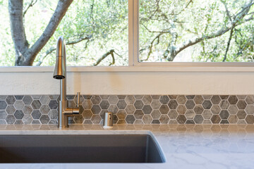 Modern kitchen detail of kitchen sink with window view of nature, and marble counter with hexagon...