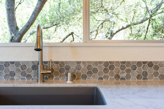 Modern Kitchen Detail Of Kitchen Sink With Window View Of Nature, And Marble Counter With Hexagon Tile Backsplash. 