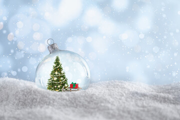 Beautiful glass ball with Christmas tree and gift on snow against light blue background, space for...