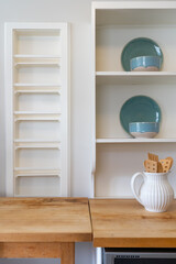 Kitchen details of wooden counters with built in magazine rack and exposed shelving with ceramic dishware. 