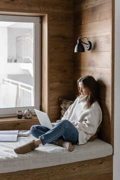 Woman using laptop on cozy window seat