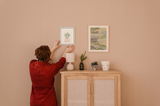 Woman adjusting frame with mosaic on wall
