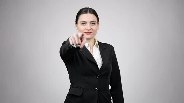 Young business woman pointing her finger at you and wearing a black suit on a grey background