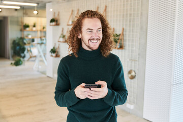 Cheerful mid adult man looking away while using mobile phone at studio apartment