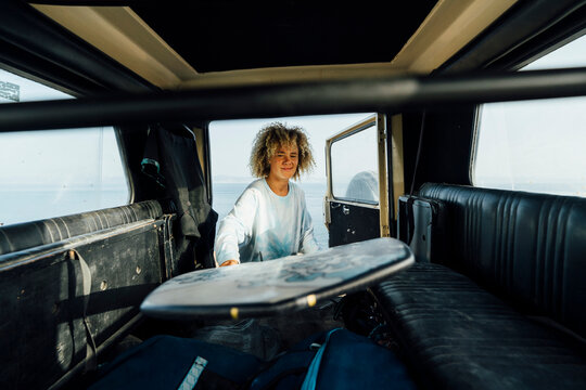 Smiling woman removing surfboard from car while standing at beach