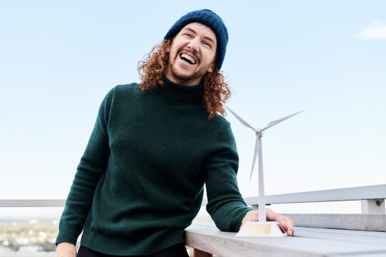Cheerful man with windmill model on building terrace against sky
