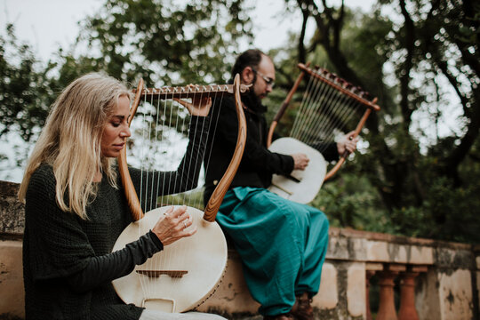 Female with male playing lyra musical instrument on bench