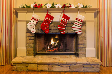 Four colorful Christmas stockings decorate a stone firesplace with a glowing fire.