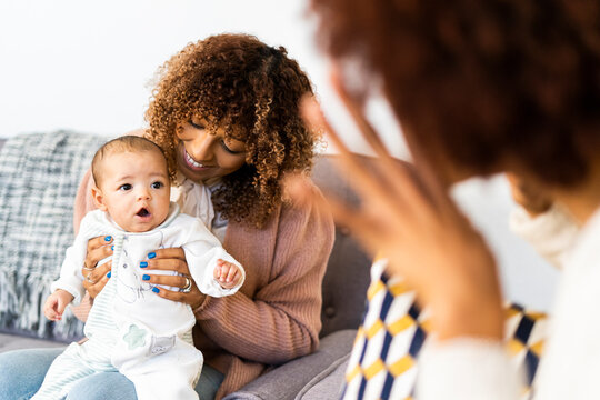 Female toddler looking at aunt doing hand gesture sitting on sofa in living room
