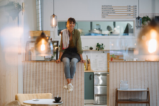Young female entrepreneur sitting on counter in coffee shop
