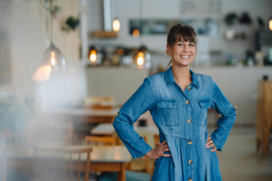 Female owner with hand on hip standing in coffee shop