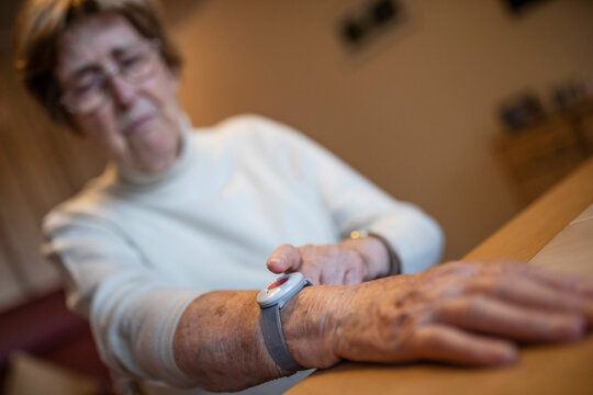 Wrinkled worried woman pressing emergency push button on wrist over table at home