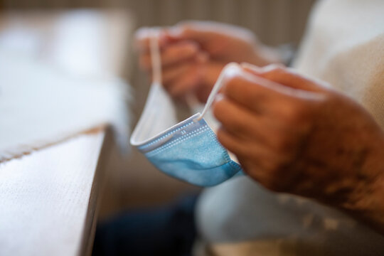 Hand of wrinkled woman holding protective face mask during lockdown at home