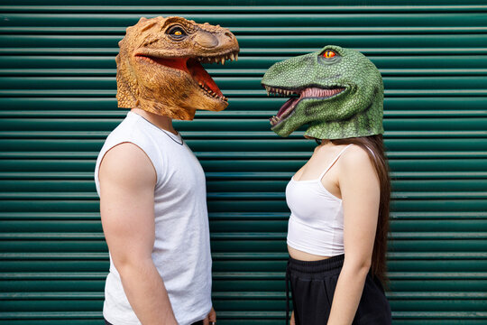 Male and female wearing dinosaur mask against green shutter