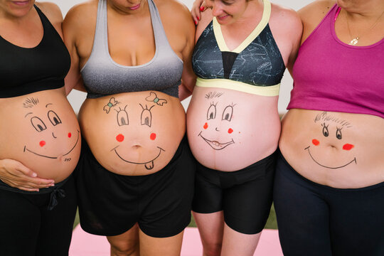 Midsection of pregnant women with face drawing on stomach standing at yoga studio