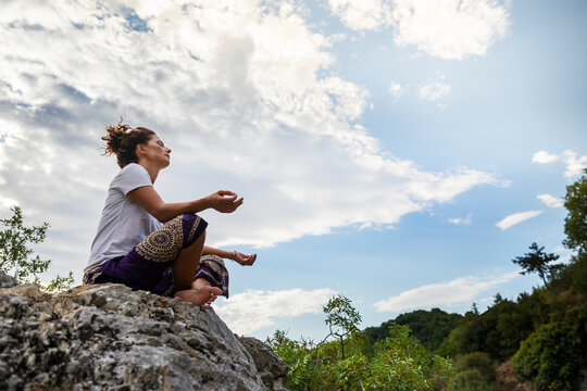 Woman meditating while sitting on rock against sky at Marmitte Dei Giganti, Marche, Italy