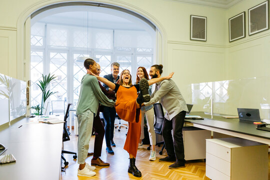 Cheerful businesswoman falling while coworkers catching at workplace