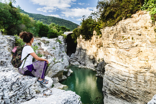 Woman looking at view of valley while sitting on rock of mountain at Marmitte Dei Giganti, Marche, Italy